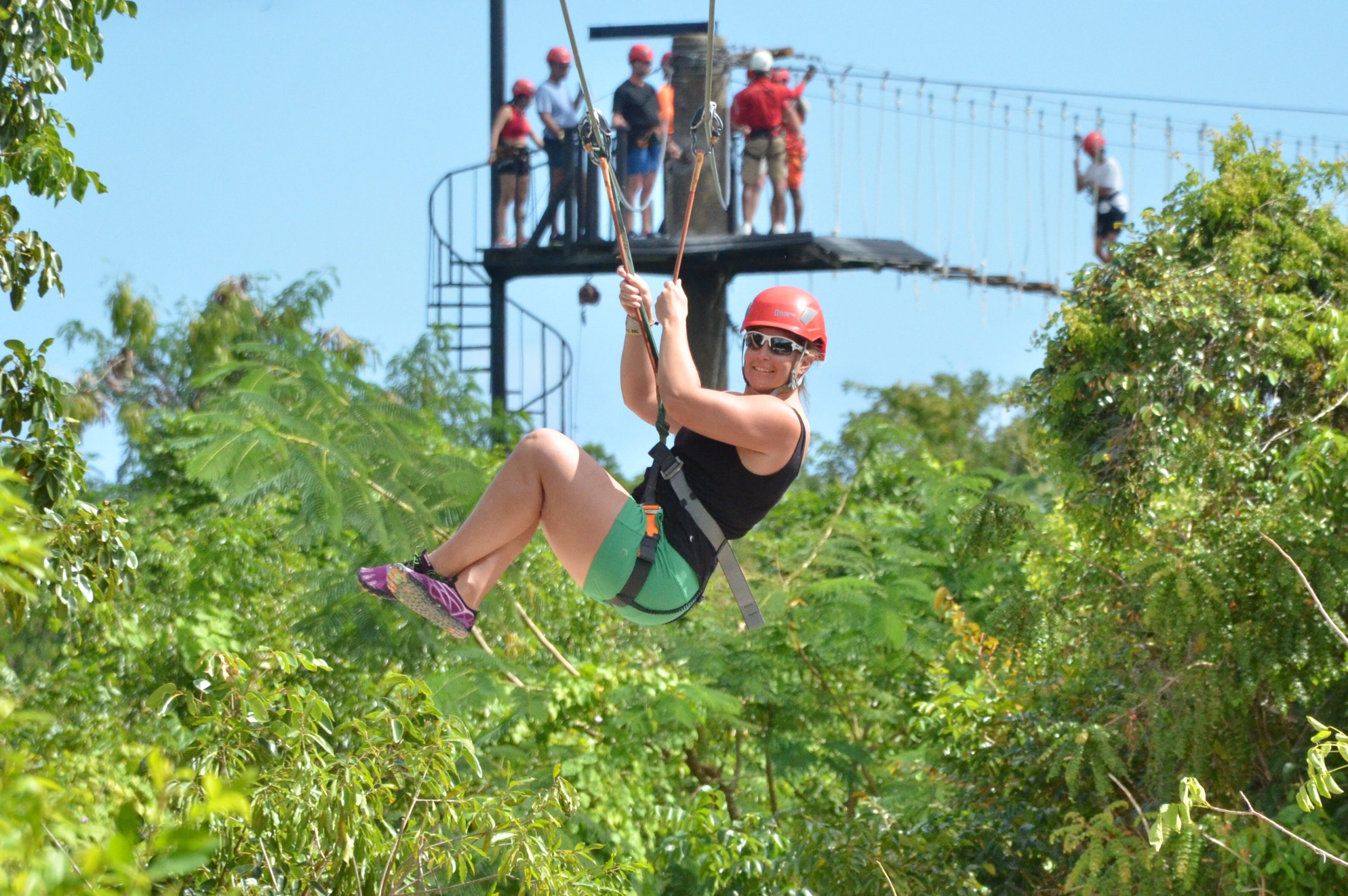 Smiling woman in red helmet ziplining over green treetops at a Punta Cana adventure park