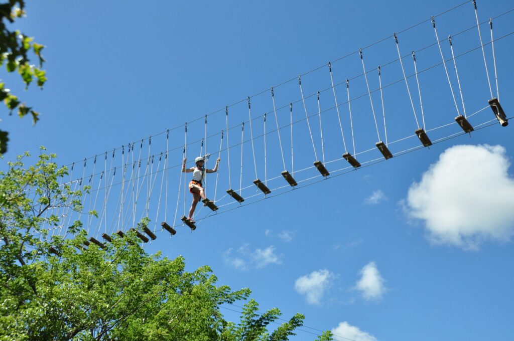 Persona cruza un puente colgante de cuerdas en un circuito de canopy bajo cielo azul