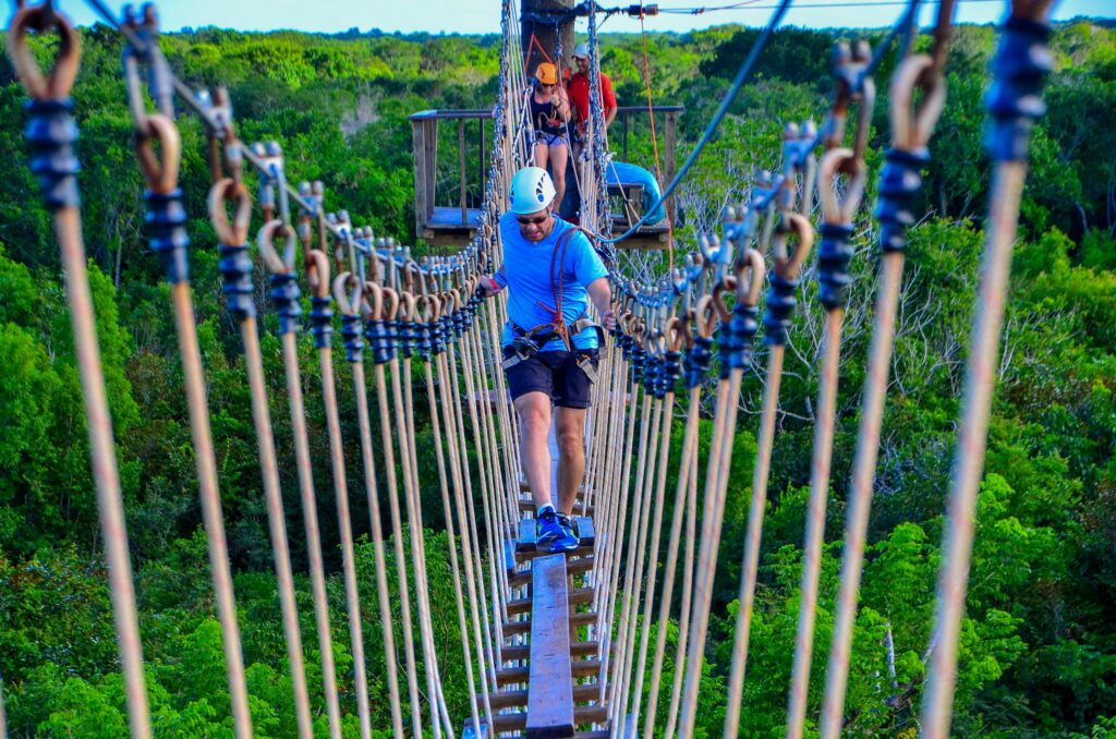 People crossing a long suspended canopy rope bridge high above the green jungle