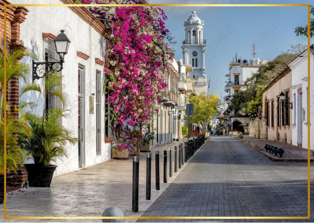 Calle colonial empedrada con buganvilias y torre de iglesia blanca en Santo Domingo