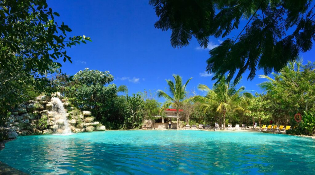 Tropical lagoon pool with a rock waterfall, palm trees and lounge chairs under blue sky