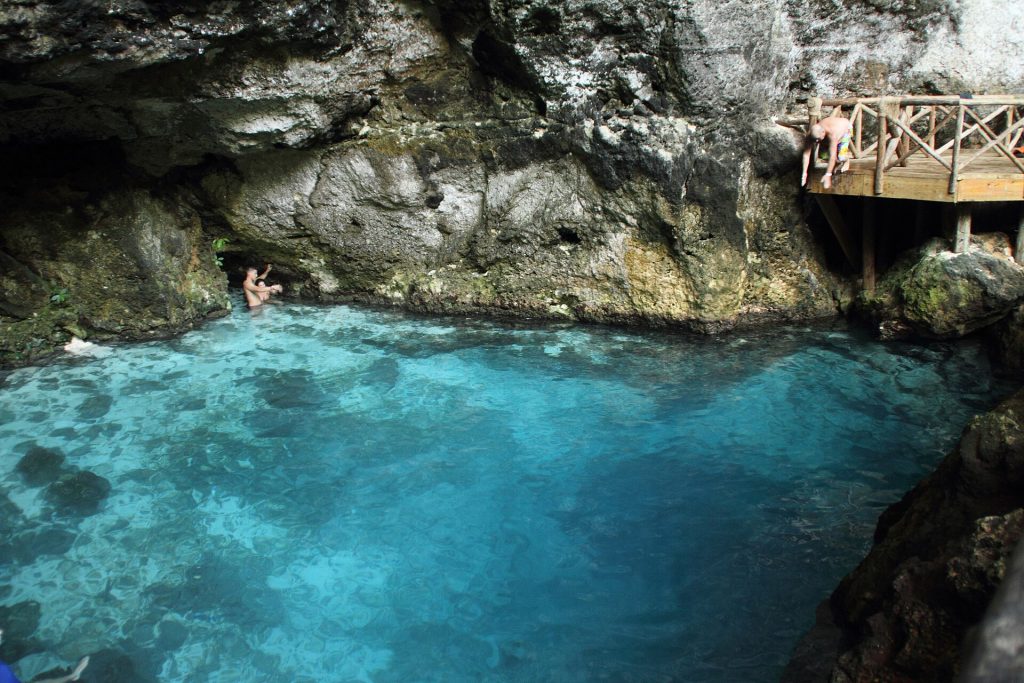 Poza natural turquesa del cenote Hoyo Azul rodeada de acantilados