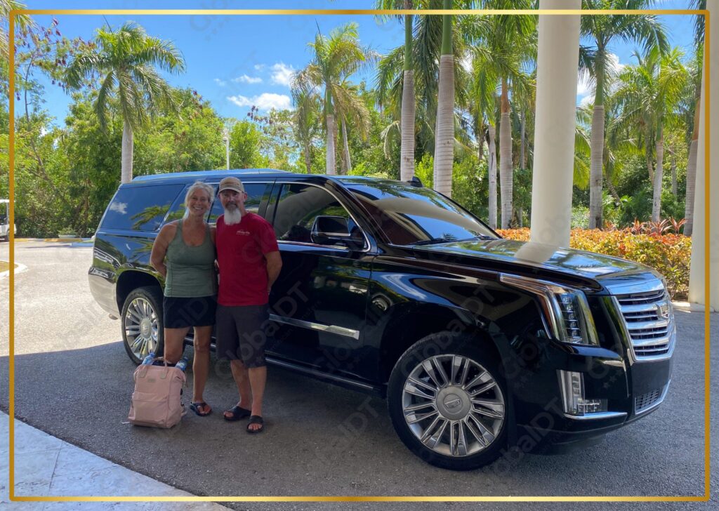 Pareja posando junto a una Cadillac Escalade negra con equipaje bajo palmeras en un traslado soleado