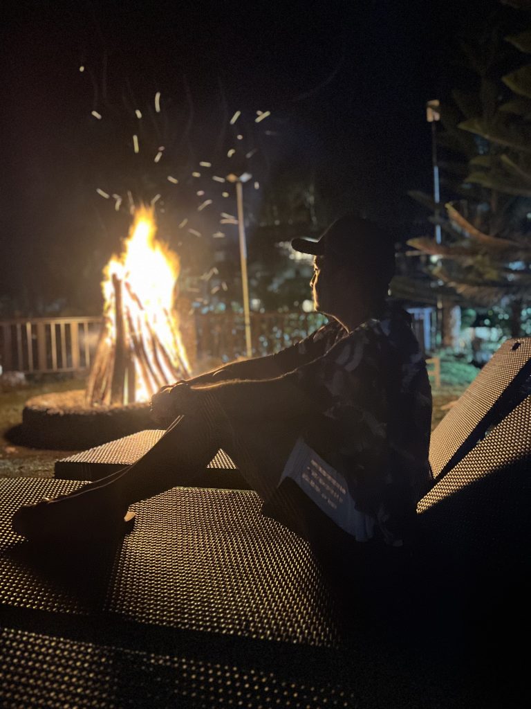 Persona sentada en una silla de playa junto a una fogata en la noche