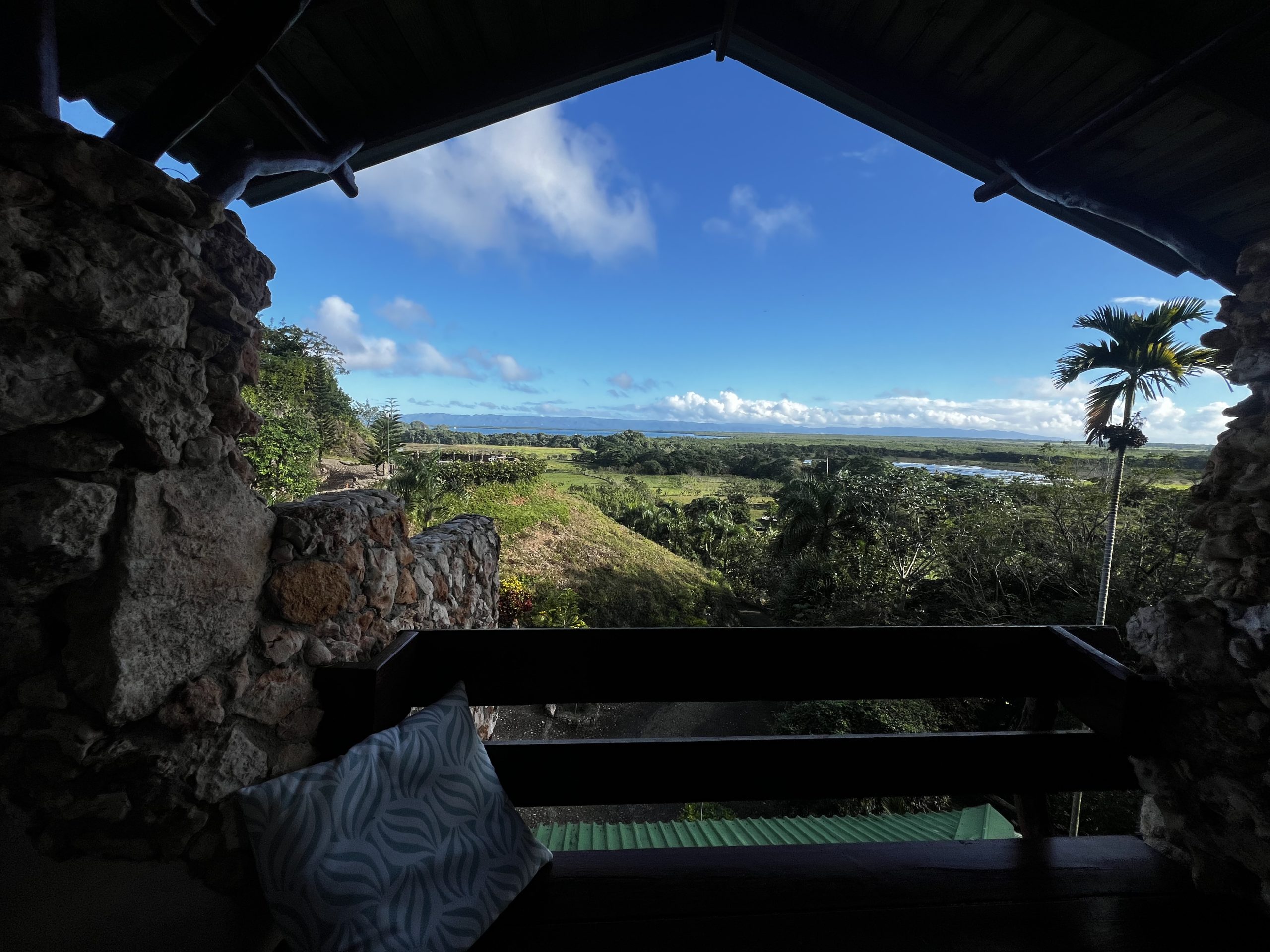 Terraza mirador de piedra con un banco, con vista a un paisaje tropical exuberante y cielo azul