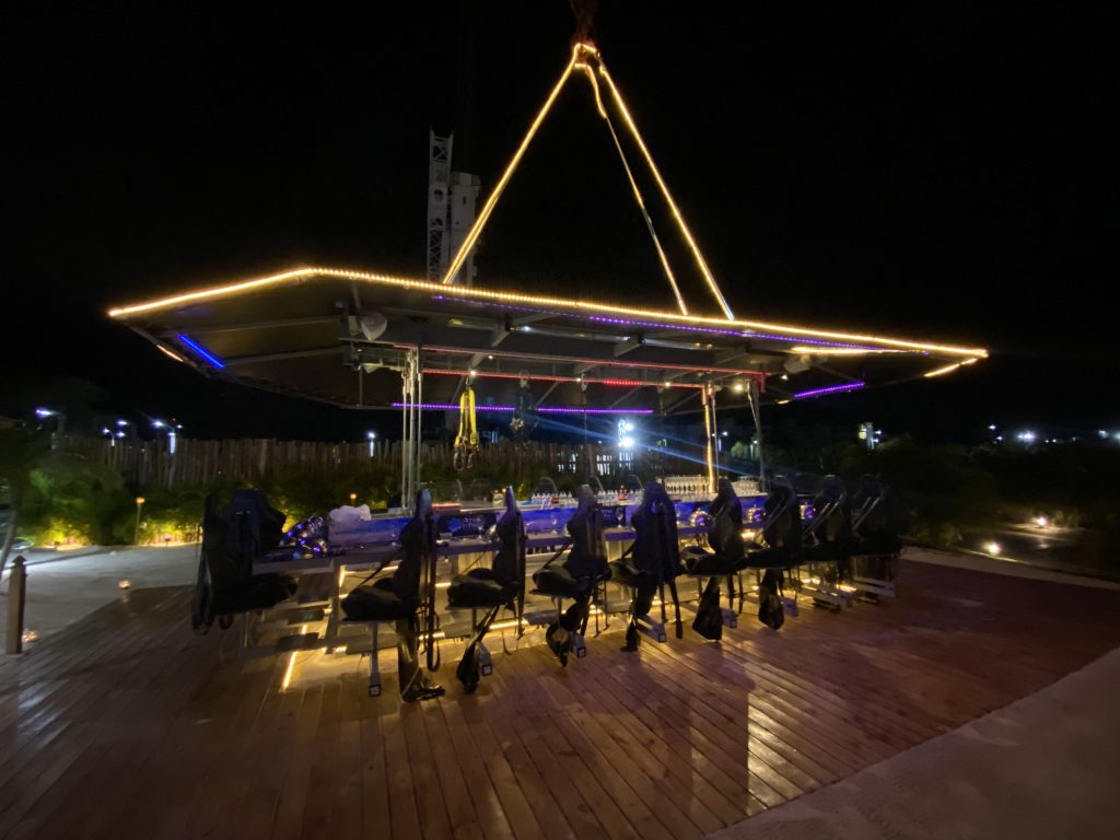 Lit outdoor deck bar with swing seats over a pool at night