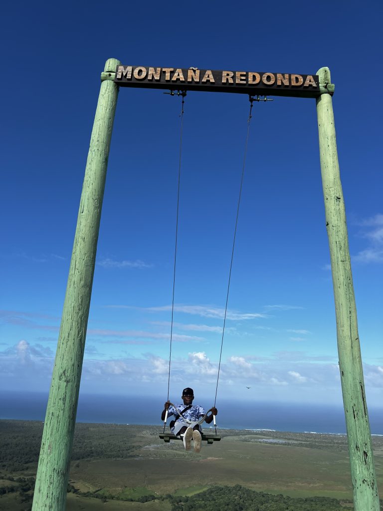 Persona en el columpio gigante de Montaña Redonda sobre las llanuras verdes de la costa