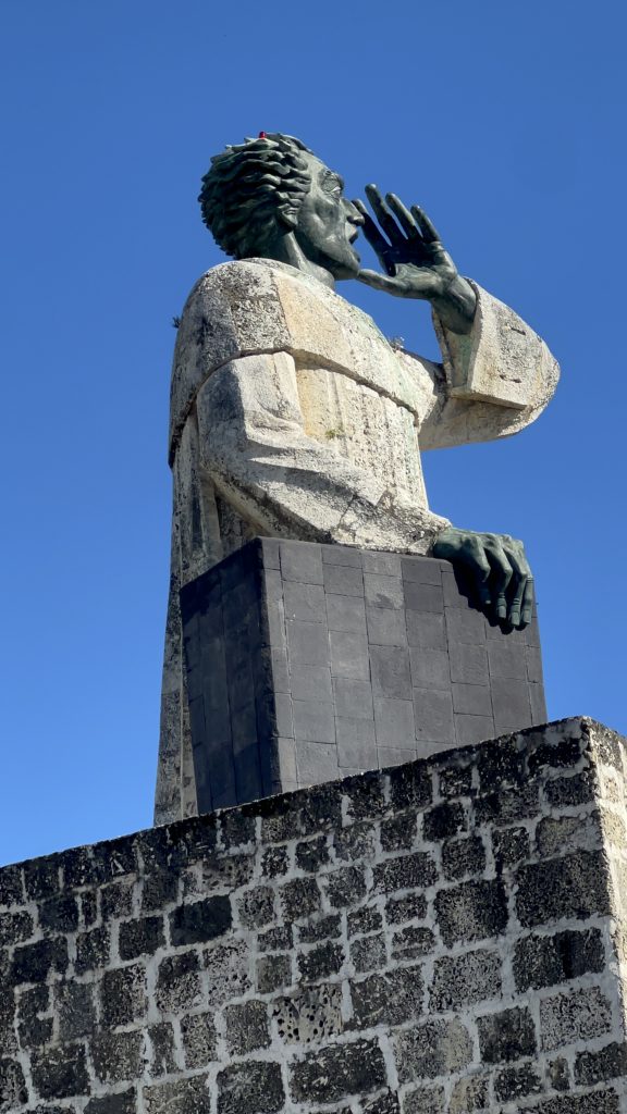 Estatua de piedra de Fray Anton de Montesinos gritando contra un cielo azul despejado
