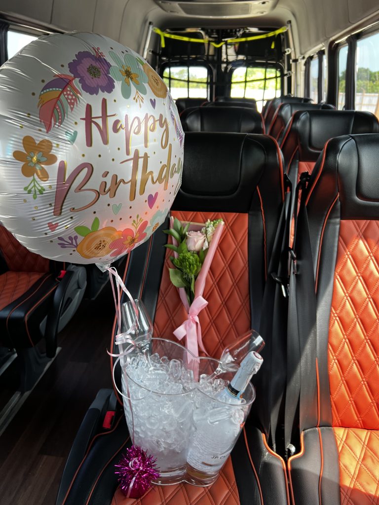 Decorated shuttle van interior with birthday balloon, flowers, and an ice bucket with champagne