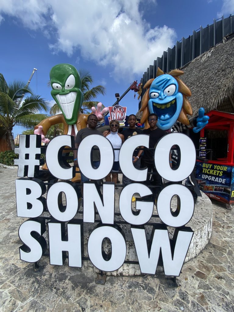 Group posing at the #COCOBONGO SHOW sign with cartoon mascots under a blue sky