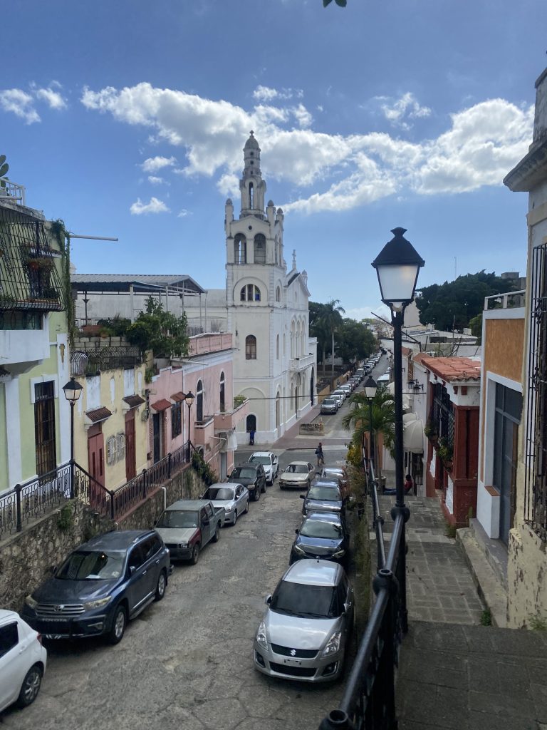 Calle colonial de Santo Domingo con iglesia blanca, farol y autos estacionados