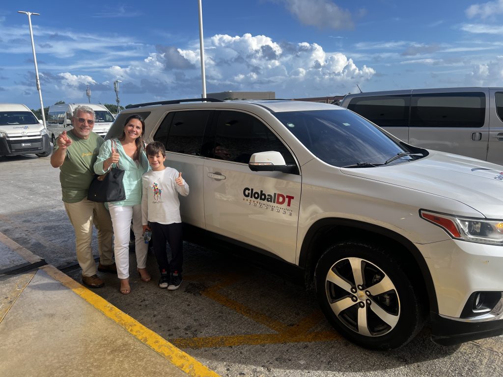 Family giving thumbs up beside a white Chevrolet Traverse GlobalDT SUV at the airport